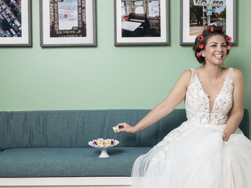 Bride in hair rollers laughing on a teal banquette