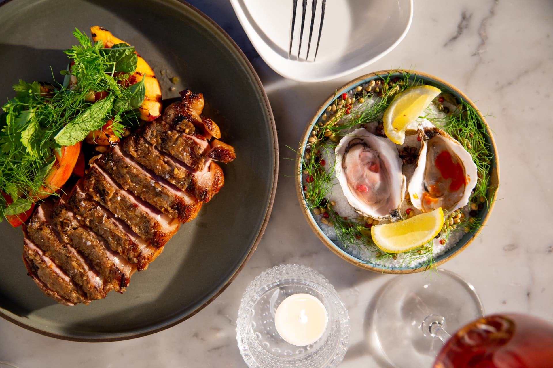 Oysters on salt with lemon beside a sliced grilled steak on a marble table
